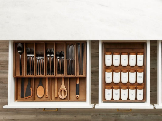 Wooden kitchen drawer organizer with dark utensils and white marble counter top