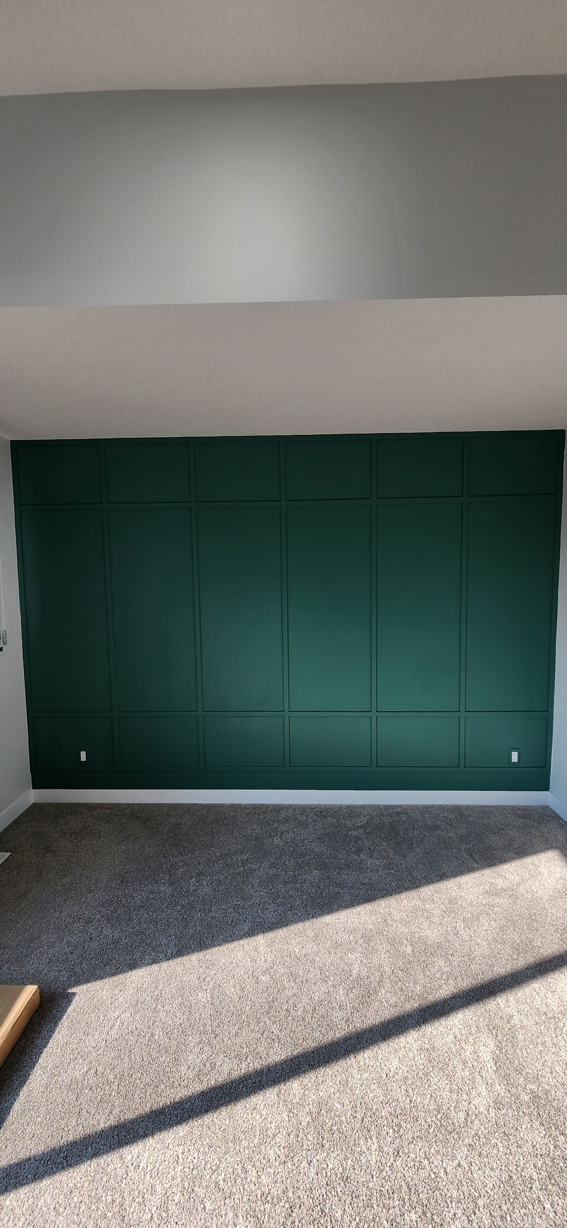 Green board and batten wall in an empty room with white walls and grey carpet