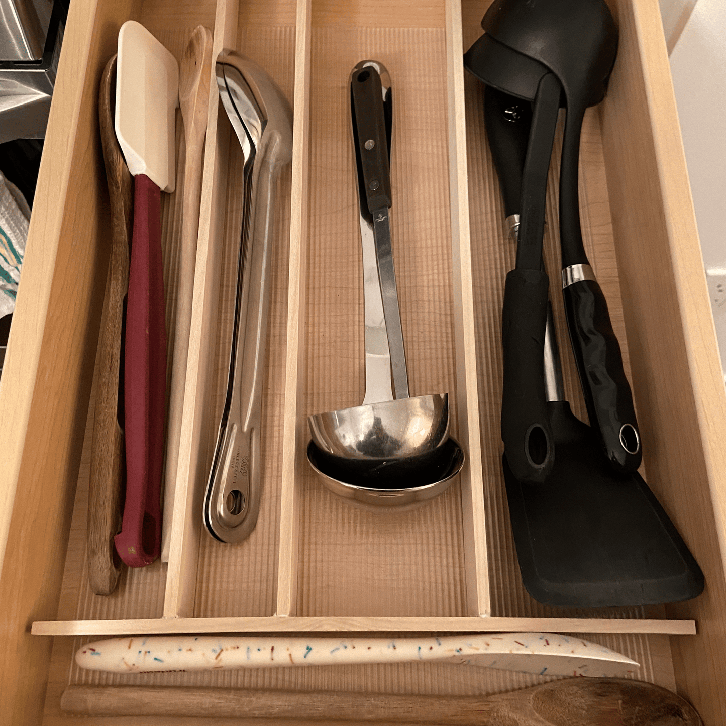 Wood dividers in a drawer with kitchen utensils.