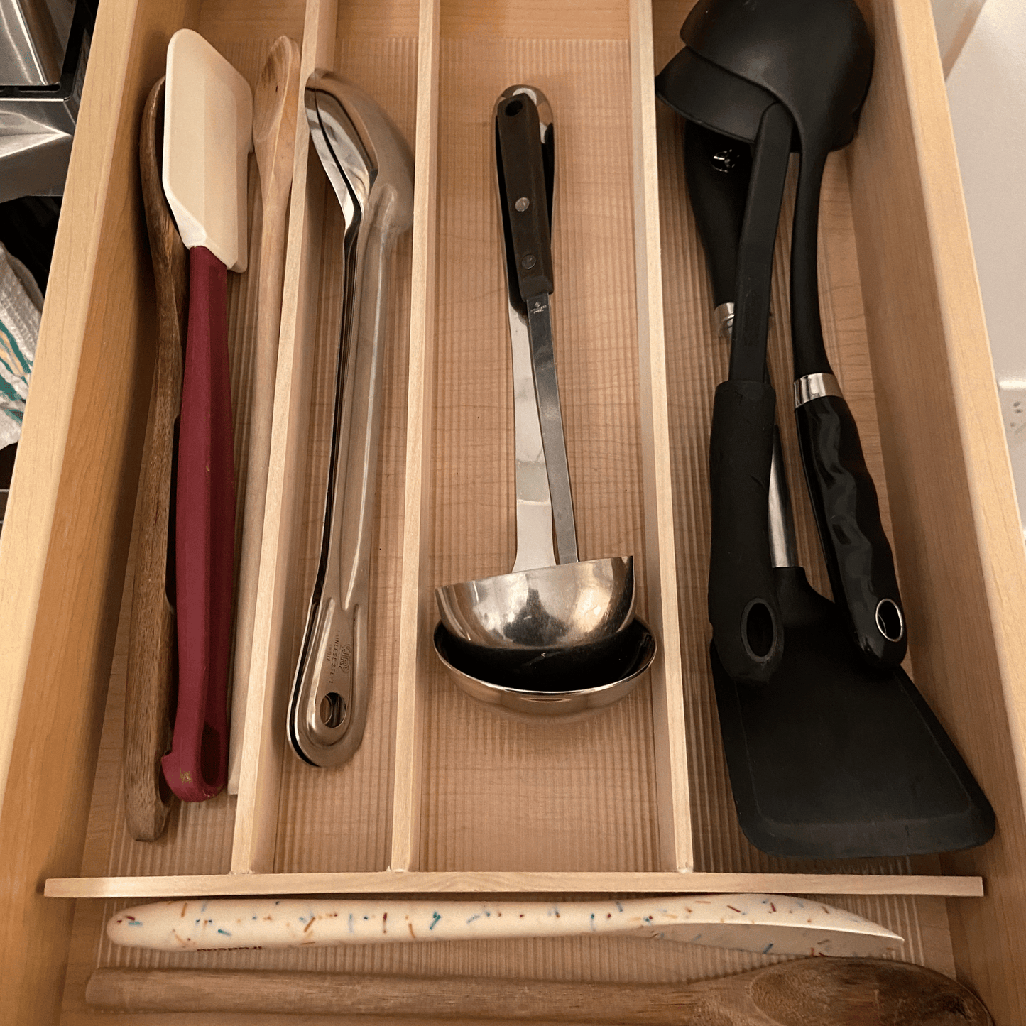 Wood dividers in a drawer with kitchen utensils.