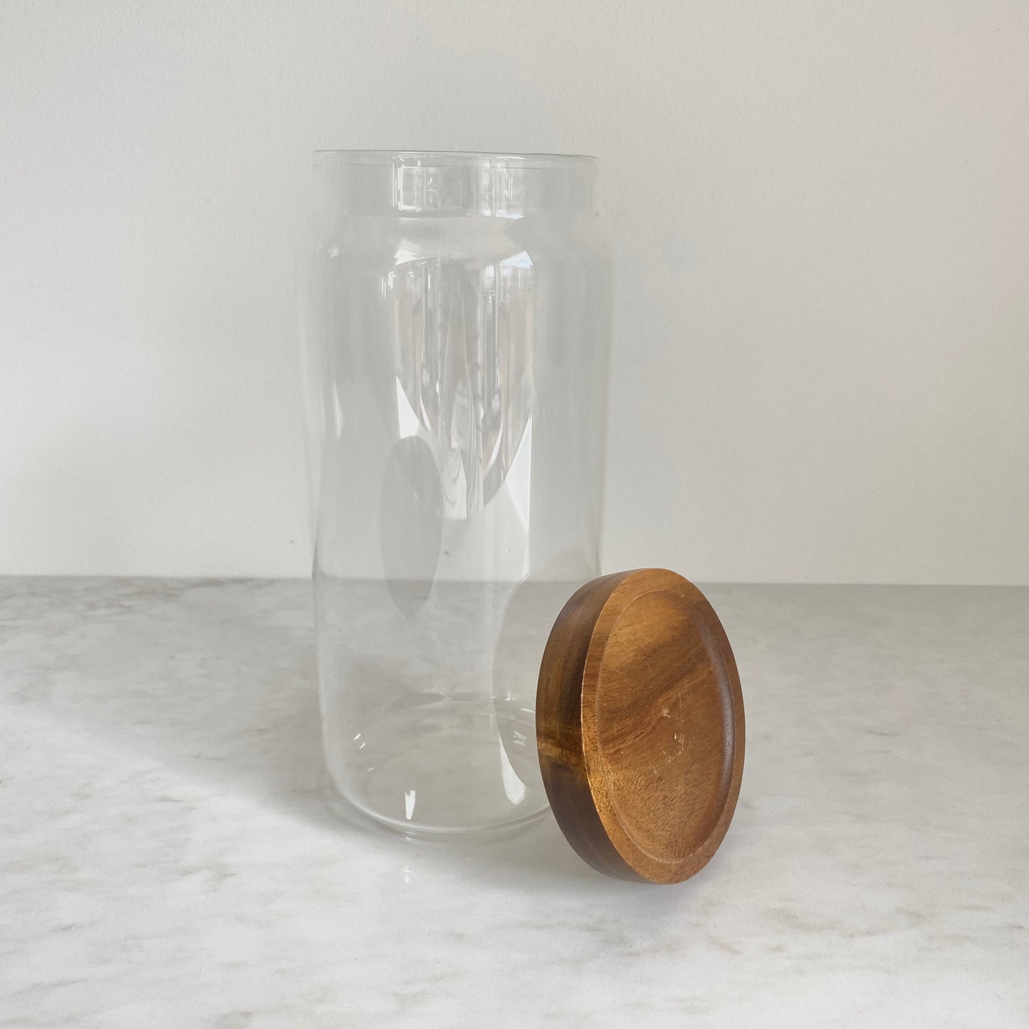 Large size glass canister with acacia wood lid resting on the side